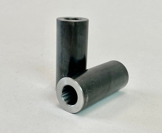 Two black cylindrical lower link bushing sleeves with metal-lined hollow centers on a white surface.