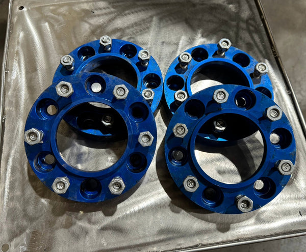 Four blue 1.25-inch Spidertrax hub-centric wheel spacers with bolts, designed for Toyota vehicles, on a metal surface.