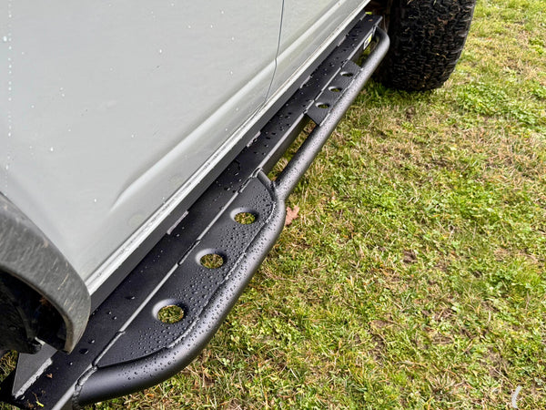 Close-up of black metal rock slider installed on the rear right side of a 2021 Ford Bronco 4-door.
