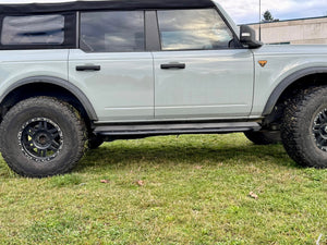 Side view of 2021 Ford Bronco 4-door with black Metal Tech rock sliders installed on grassy ground.