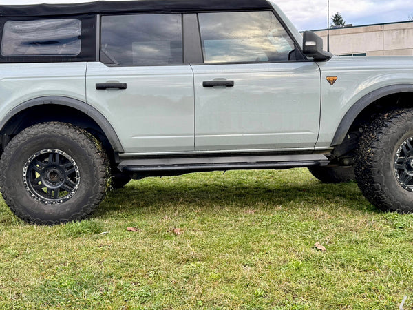 Side view of 2021 Ford Bronco 4-door with black Metal Tech rock sliders installed on grassy ground.