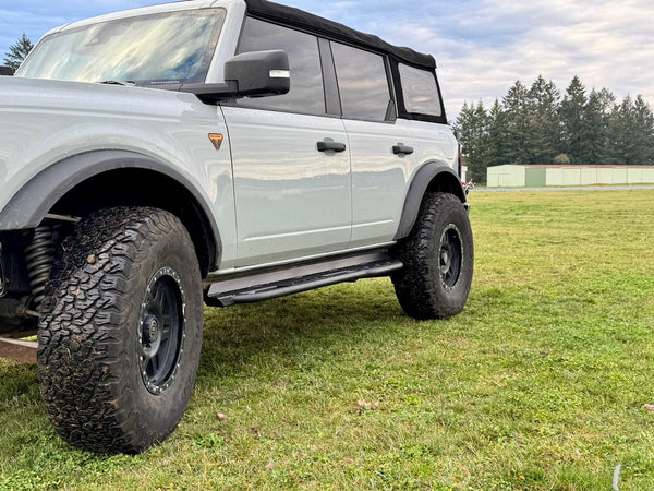 2021 Ford Bronco 4-door with black Metal Tech RRR rock sliders installed on grassy field side view.