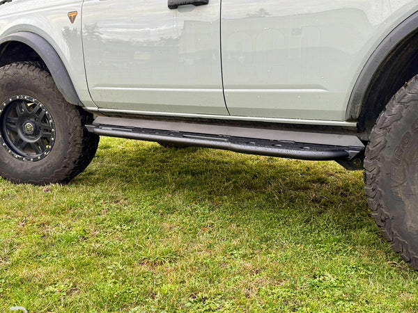 Close-up side view of black rock sliders installed on a 2021 Ford Bronco 4-door on grass.