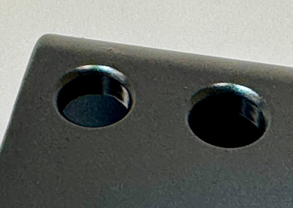 Close-up of black metal rear bump stop drop plate with two circular mounting holes for long travel suspension.