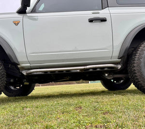 Side view of 2021 Ford Bronco 2-door with installed Sidewinder RRR rock sliders by Metal Tech 4x4 on grassy ground.