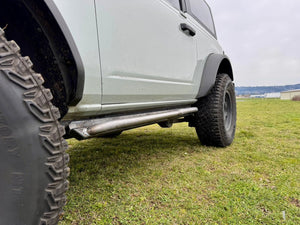 Close-up side view of 2021 Ford Bronco 2-door with raw metal Sidewinder RRR rock sliders installed above grass.