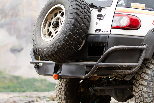 Close-up of black metal tube rear bumper installed on white FJ Cruiser with spare tire and off-road decals.
