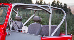 Close-up of raw metal roll cage installed on red FJ40 Land Cruiser with black seats and forest background.