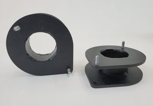 Pair of black metal front spacer plates with bolts for vehicle suspension lift installation.
