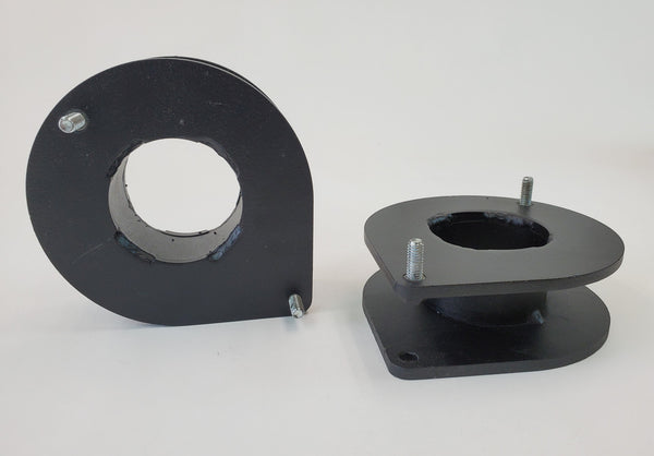 Pair of black metal front spacer plates with bolts for vehicle suspension lift installation.