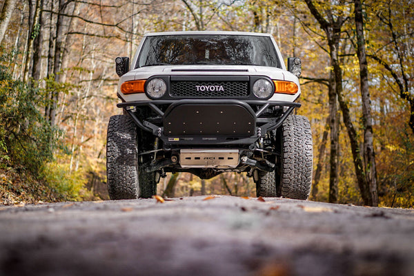 Front view of white Toyota FJ Cruiser with Metal Tech black front tube bumper installed on forest road.