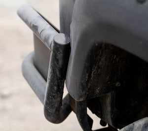 Close-up of black metal tube rear bumper installed on a dusty vehicle corner, showing sturdy welded joints.
