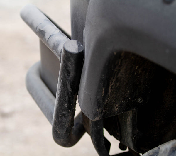 Close-up of black metal tube rear bumper installed on a dusty vehicle corner, showing sturdy welded joints.