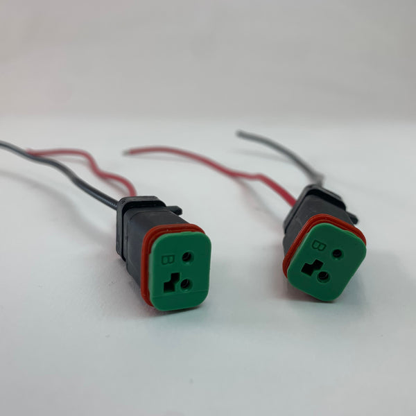 Pair of black Deutsch DT LED plugs with green faces and red seals, each with bare red and black wires.
