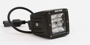 Close-up of OPOR 20W LED pod light with flood beam pattern and attached power cable on white background.