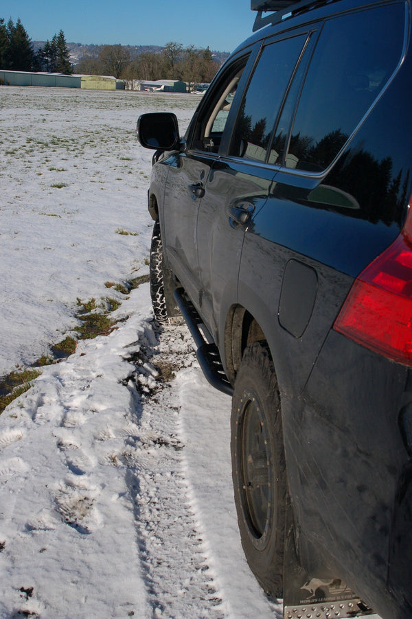 Black Lexus GX460 with Metal Tech 4x4 rock sliders installed, driving on snowy terrain.