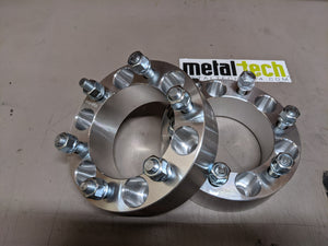 Pair of 6x5.5 bolt pattern, 2-inch thick aluminum wheel spacers with lug studs and nuts on a gray surface.