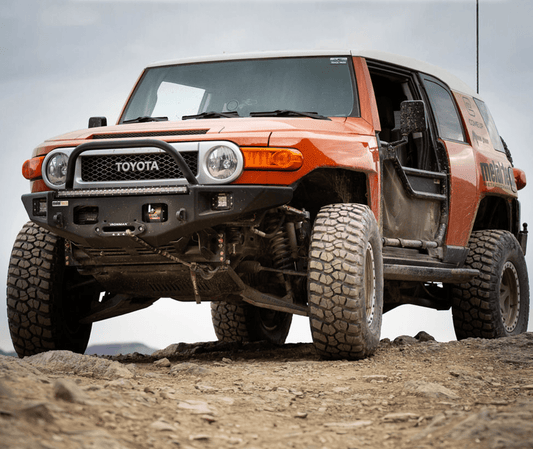 Orange Toyota FJ Cruiser with Metal Tech Phantom front bumper and off-road tires on rocky terrain.