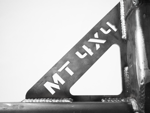 Close-up of welded metal bracket with "MT 4X4" cutout on Bronco 6G rear bumper swing arm system.