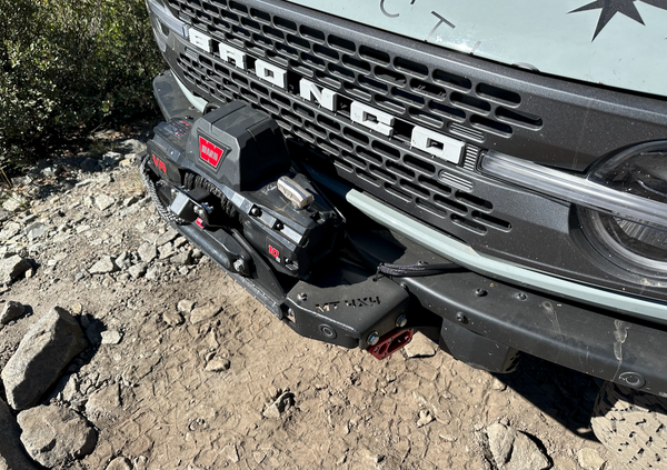 Front camera relocation kit installed on Ford Bronco 6G bumper with winch and off-road terrain background.