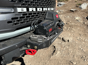 Close-up of Bronco 6G front bumper showing installed front camera relocation kit with winch and red mounting bracket.