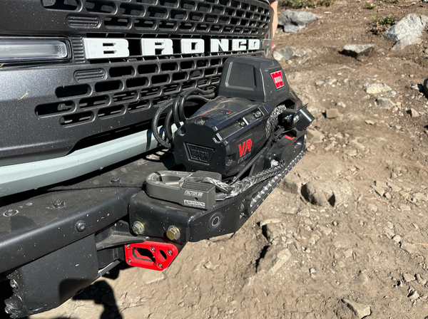 Close-up of Bronco 6G front bumper showing installed front camera relocation kit with winch and red mounting bracket.