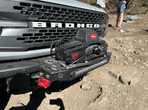 Close-up of Bronco 6G front bumper with winch and relocated front camera on off-road dirt trail.
