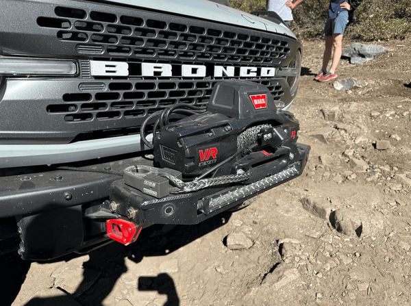 Close-up of Bronco 6G front bumper with winch and relocated front camera on off-road dirt trail.