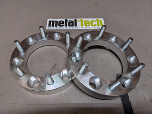 Pair of 6x5.5 1-inch hub-centric aluminum wheel spacers with studs, shown inside an open box on a work surface.
