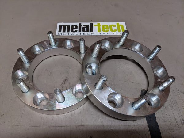Pair of 6x5.5 1-inch hub-centric aluminum wheel spacers with studs, shown inside an open box on a work surface.