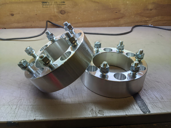 Two silver 6x5.5 hubcentric wheel spacers with bolts on a workbench, shown out of the box.