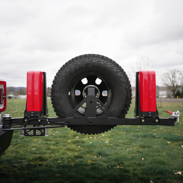 Bronco 6G rear bumper with Ace of Hearts swing arm system holding a spare tire and two red fuel cans outdoors.