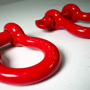 Close-up of a pair of red powder-coated metal shackles on a white surface.