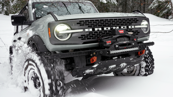 Front view of a gray Bronco 6G with Stronghold winch mount and winch driving through snow.