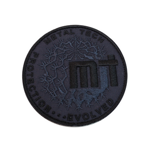 Round black embroidered morale patch with "Metal Tech Protection Evolved" text and barbed wire design.