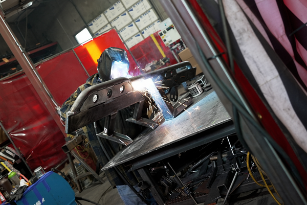 Welder fabricating Metal Tech rock sliders for 2021 Ford Bronco 4-door, sparks flying in workshop setting.
