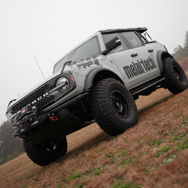Front angle of a white Bronco 6G with a Stronghold winch mount and off-road tires on grass.